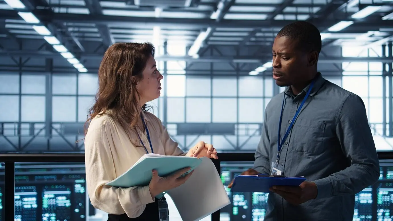 Gut gelaunte Admins treffen sich im Rechenzentrum, um Berichte zu prüfen, und geben sich dabei die Hand.